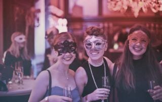 Image of three women wearing masks for Mardi Gras at a restaurant